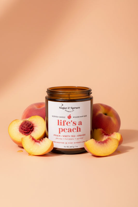 Candle labeled 'life's a peach' with peaches around on a beige background