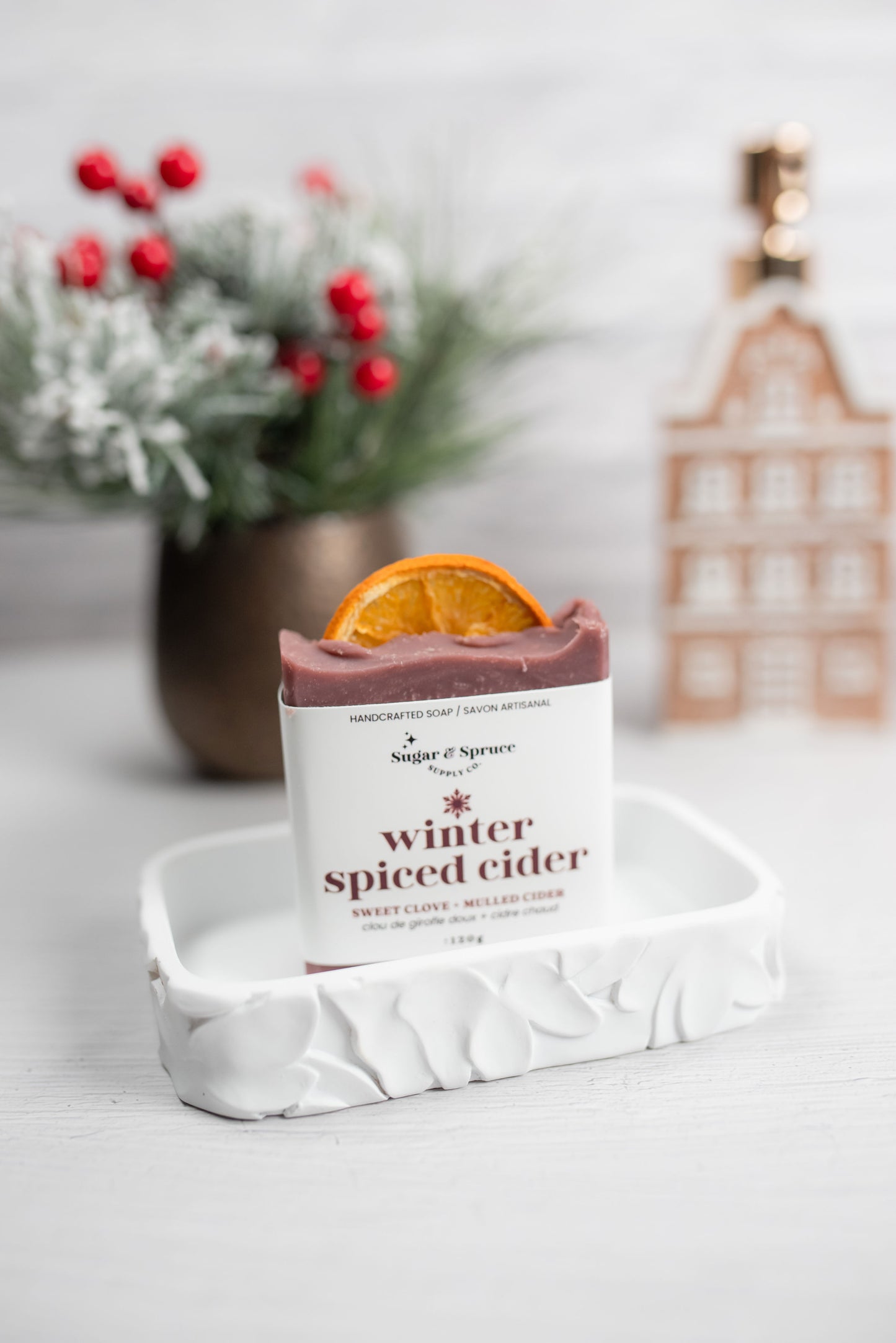 Bar of soap with an orange slice on top, labeled 'winter spiced cider', on a white marble tray with a decorative background.